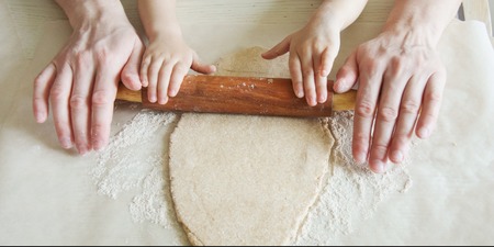 Father teaches a child to roll a dough for biscuit with a rolling pin. Hands of an adult and...