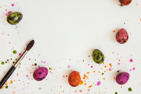 Hand-painted quail eggs with paints and a brush on the background of white paper with splashes and drops. Top view, flat lay. Copy space for text.の写真素材