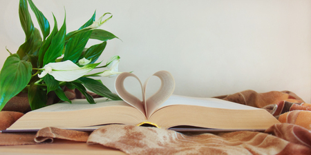 Open book with heart shape from paper pages on wardrobe, drapery woolen stole, blooming spathiphyllum. Concept of home comfort. Banner. Copy space, front view.の写真素材