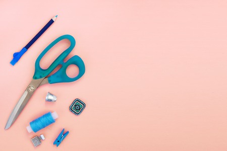 Accessories and tools for sewing scissors, pencil, thimble, thread reel, clothespin, foot for sewing machine, plain blue on a pink background. Top view, flat lay. Copy space for text.の写真素材
