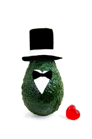 Fresh avocado in an elegant suit of black and white hats, shirts and bow ties with red glass heart isolated on white background. Minimal concept for wedding holidays card, invitations. Front view.の写真素材