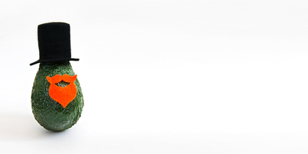 Fresh avocado in an elegant suit of black hat, beard and mustache on bright background. Minimal concept for wedding holidays card, party invitations. Front view, web banner, copy spaceの写真素材