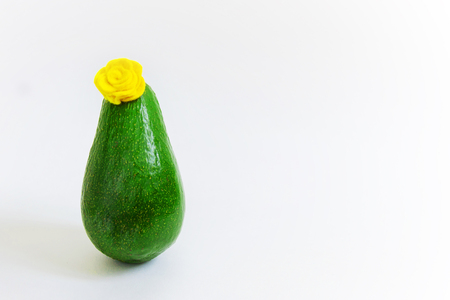 Slender fresh green avocado with a flower hat like an elegant woman. Minimal original vegan concept for party invitations and holidays greeting cards. Copy space, front view, isolated on whiteの写真素材