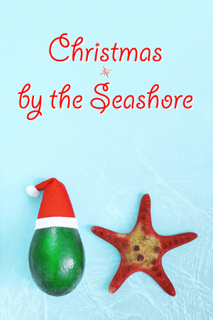 Fresh green avocado in a red hat next to a starfish and sweet candy cane on a bright blue background with water texture. Christmas concept, poster, tourist advertisements. Top view, templateの写真素材