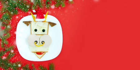 Funny Christmas sandwich for a child or party in the form of bull (sausage, bread, vegetables). With branches of Christmas trees and decorations, top view, copy spaceの写真素材
