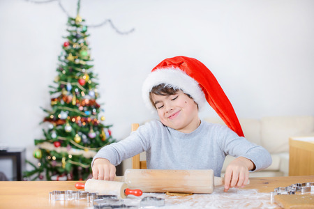 Cute child is rolling dough with Christmas tree behindの写真素材