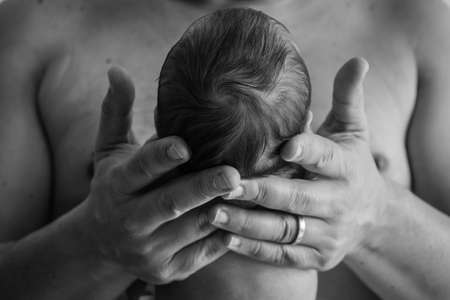 Dad holding his newborn baby in his hands, man's hands holding baby's head.の写真素材