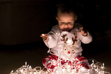 Tarragona, Spain - December 3, 2017: Cute baby girl wearing a reindeer pajama playing with Christmas lights.のeditorial素材