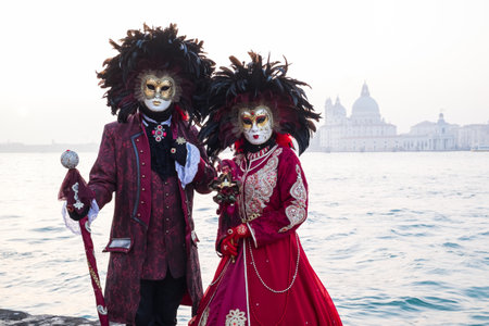 Venice, Italy - February 18, 2020: An unidentified couple in a carnival costume in front of Santa Maria della Salute, attends at the Carnival of Venice.のeditorial素材