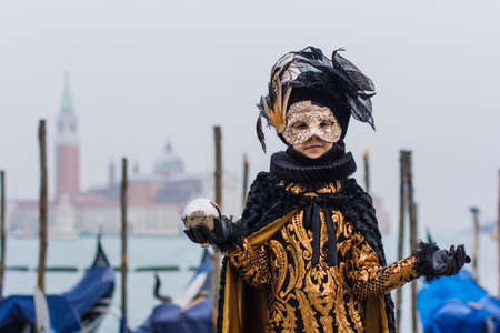 Venice, Italy - February 18, 2020: An unidentified ki in a carnival costume in front of a group of gondolas and St Giorgio's Island, attends at the Carnival of Venice.のeditorial素材