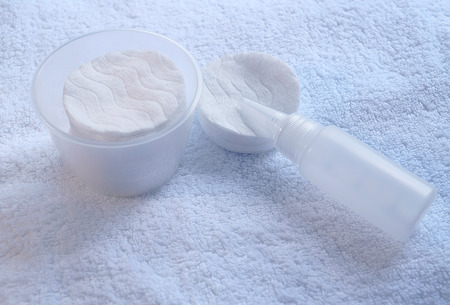 Cotton hygienic pads in matte translucent case, small bottle against a background white terry towel. Drop lotion, care cream or medicine leaked onto cotton disc flows out of the bottle spout.の写真素材
