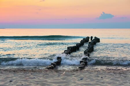 breakwaters in the sea at sunrise, sunset on the seashore