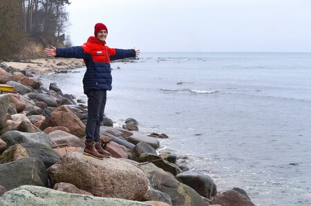 young man standing on sea stones, man on the seashore with his hands up, Baltic sea, Kaliningrad region, Russia, December 30, 2018のeditorial素材