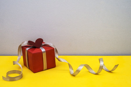 gift in red packaging with silver gray ribbon, valentine's day accessory, gray and yellow background, valentine's day decoration on February 14の写真素材
