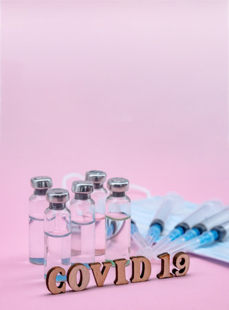 Prevention of seasonal diseases. Medical ampoules, syringes and a mask on a pink background. Vaccination against covid-19.の写真素材
