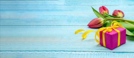 A gift and tulips on a wooden background. Spring flowers and a gift box. Red tulips and red...