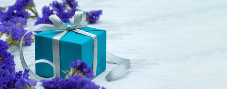 Gift wrap and blue flowers. A blue box with a gray ribbon. Blue gift box on wooden background.