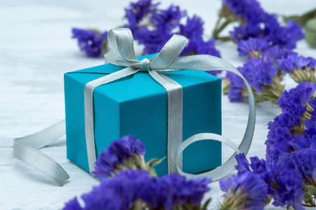 Gift wrap and blue flowers. A blue box with a gray ribbon. Blue gift box on wooden background.