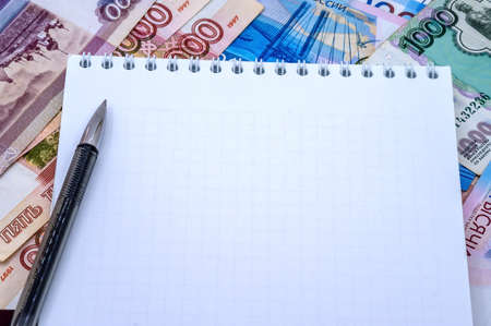 A clean slate against the backdrop of money. Rubles notebook and black pen. Notepad on a spring and a pen.の写真素材
