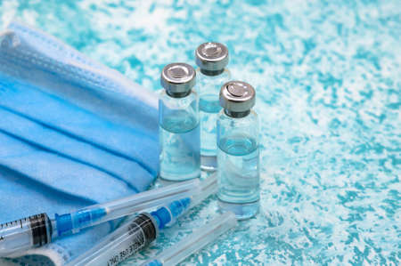Medical vials, syringes and mask on a green background. Prevention of seasonal diseases. Vaccination against covid-19.の写真素材