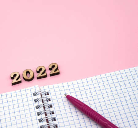 Wooden numbers 2022. Notepad on a spring. Notepad and Pen on Pink. Pink Pen. Spiral spiral checkered sheets.の写真素材