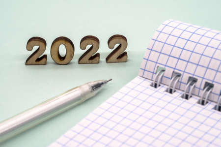 Notebook and pen on the table. Wooden numbers 2022. A blank sheet of paper and a ballpoint pen.
