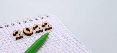 Notebook and pen on the blue. Wooden numbers date 2022. A blank sheet of paper and a green pen.の写真素材