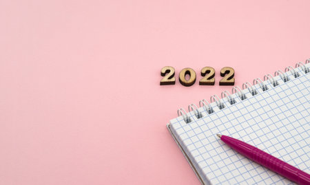 Wooden numbers 2022. Notepad on a spring. Notepad and Pen on Pink. Pink Pen. Spiral spiral checkered sheets.の写真素材