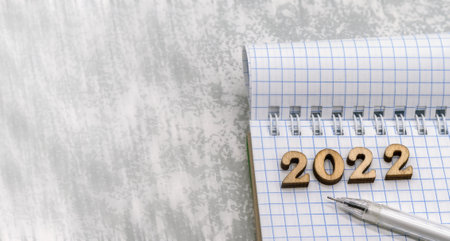 Notebook and pen on the gray. Wooden numbers date 2022. A blank sheet of paper and a white pen.の写真素材