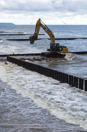 Kaliningrad region, Baltic Sea, Russia, November 29, 2020. Construction of breakwaters in the sea. Construction equipment and machinery on the seashore.のeditorial素材