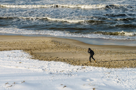 Kaliningrad, Baltic Sea, Russia, January 31, 2021. A man walks along the sea shore. Snow and wind on the sea shore.のeditorial素材
