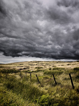 Intense looking clouds over a rural moorland. There is a poorly constructed fence running through the image.の写真素材