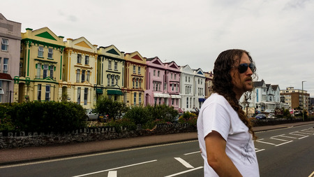 A man with long hair standing in front of a row of multicoloured houses.の写真素材