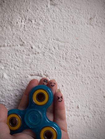 A motionless fidget spinner in a hand with smiling faces on the last three fingersの写真素材