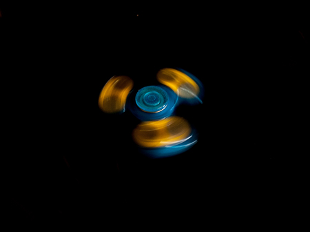 A blue and yellow fidget spinner spins on a black backgroundの写真素材