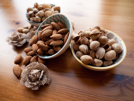Three bowls containing pistachio and almond nuts on a wooden surface