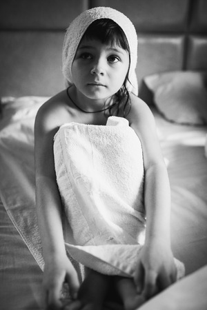 Washed the girl in a towel sitting on a white bedの写真素材