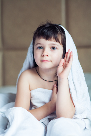Washed the girl in a towel sitting on a white bedの写真素材