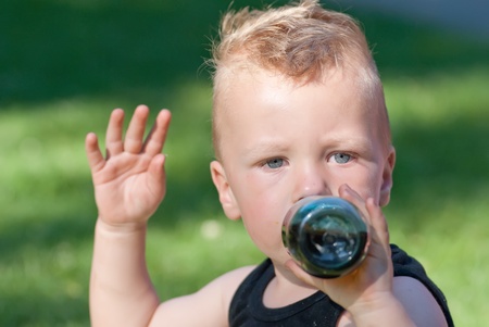 a caucasian boy drinking from a baby bottle while beckoning in the cameraの写真素材