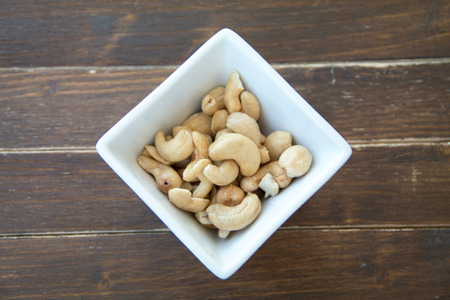 cashew nuts inside white bowl on a wooden table viewed from aboveの写真素材