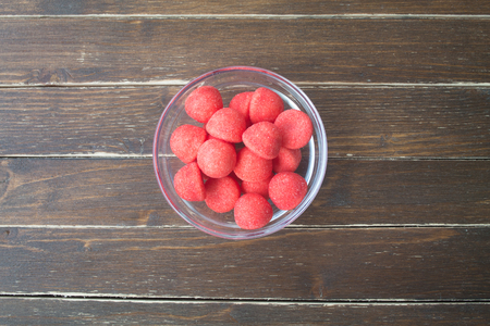 red gummy candies inside transparent bowl on a wooden table viewed from aboveの写真素材