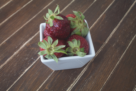strawberries inside white bowl on a wooden table viewed from close upの写真素材