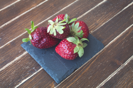 strawberries on slate on a wooden table viewed from close upの写真素材