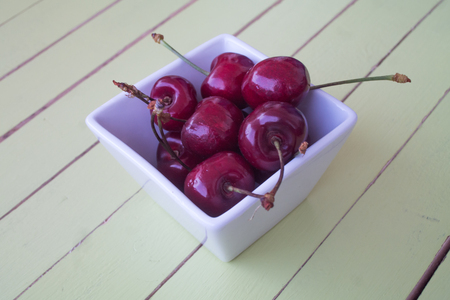 cherries inside bowl on a green wooden table viewed from close upの写真素材