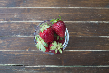 strawberries inside transparent bowl on a wooden table viewed from aboveの写真素材