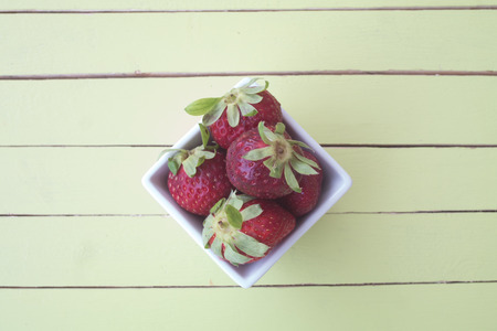 strawberries inside white bowl on a green wooden table viewed from aboveの写真素材