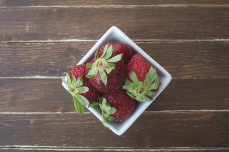 strawberries inside white bowl on a wooden table viewed from aboveの写真素材