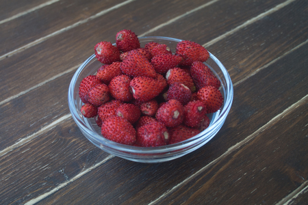 strawberries in transparent bowl on a wooden table viewed from close upの写真素材