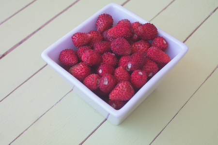 strawberries in square bowl on a green wooden table viewed from close upの写真素材