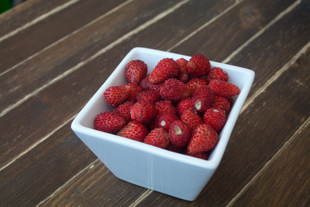 strawberries in a square bowl on a wooden table viewed from close upの写真素材